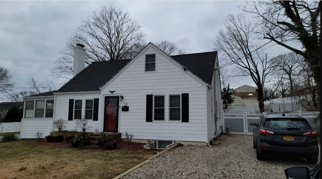 White house with black shutters, red door, and a car parked in the gravel driveway. Overcast sky.