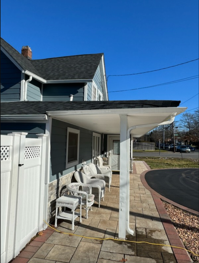 Outdoor seating area under a white canopy attached to a blue house on a sunny day.