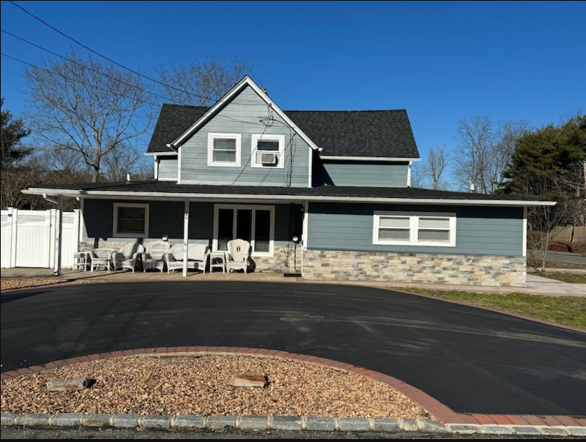 After: two-story home with new blue siding, black architectural shingle roof and stone veneer