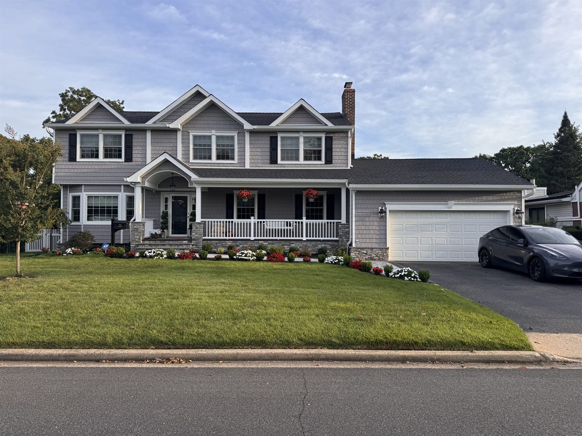 After: the same colonial with gray shake siding, three new gables, a new roof, stone veneer and a columned front porch