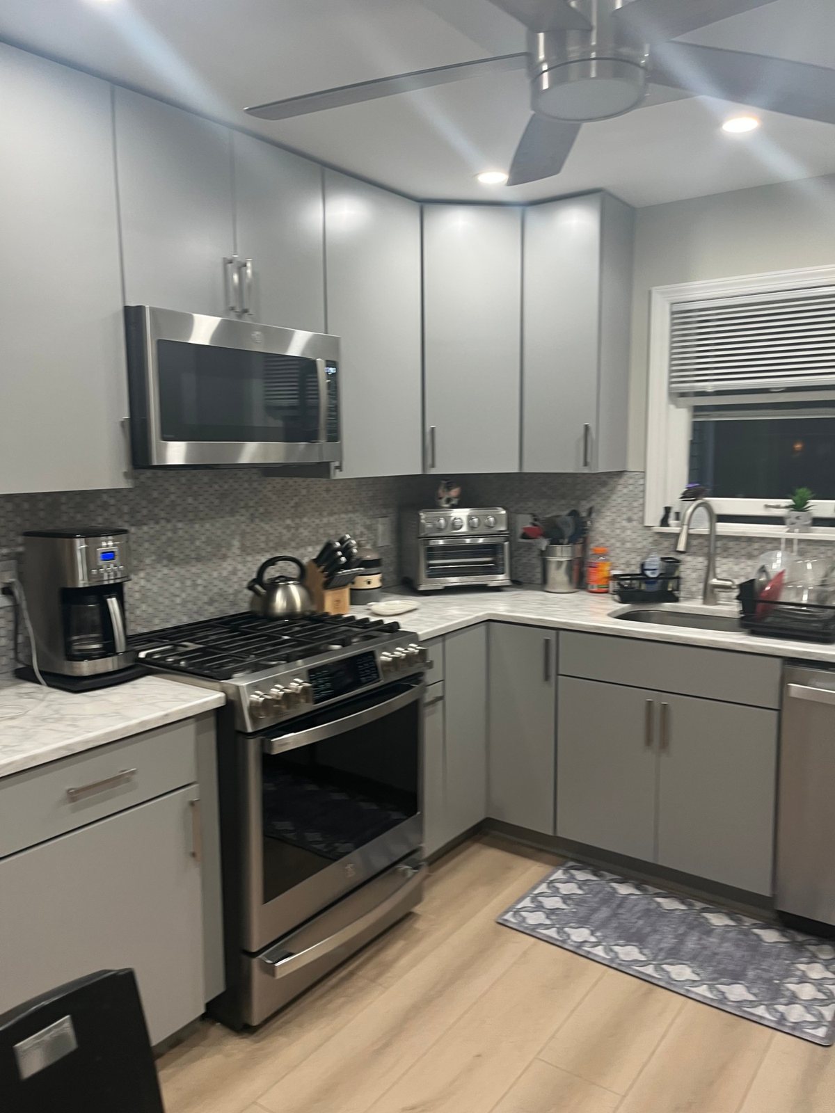 After: the same Bellmore kitchen with flat grey cabinets, marble-look quartz counters, a mosaic tile backsplash, new stainless range and microwave and light plank flooring