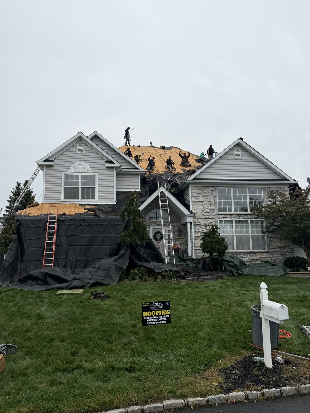 Mid-job in Holtsville, NY: the L.I. Taylor crew on the bare roof deck after tear-off, with the siding, windows and plantings wrapped in protective tarps