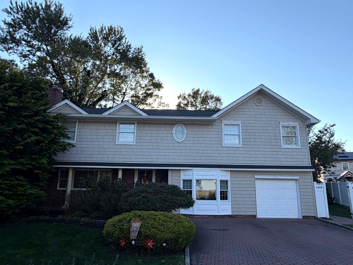 Finished job in Port Jefferson, NY: two-story home with shake-style siding, two front dormers and a new black architectural shingle roof, October 2026
