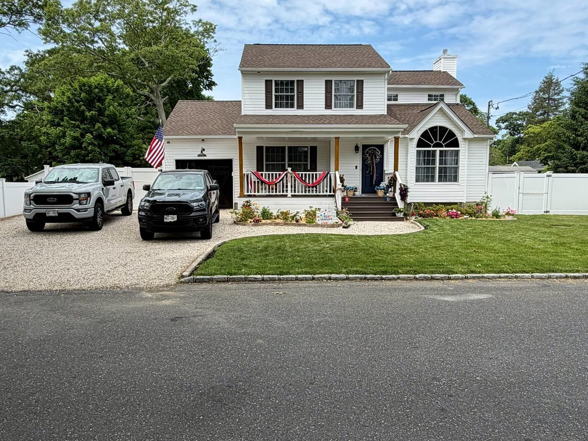 After: two-story colonial in Rocky Point with a new brown architectural shingle roof, rebuilt front porch with columns and railings, new walkway and lawn