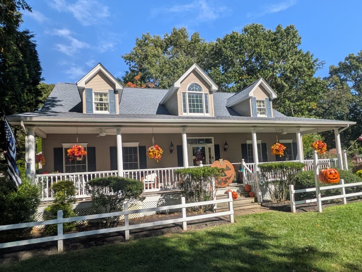 Finished job in Southold, NY: cape with three front dormers, a full-width front porch and a new light grey architectural shingle roof, October 2026
